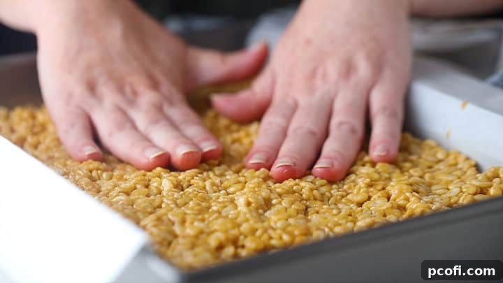 Pressing scotcheroos into a 9x13 pan, ensuring a firm, even base.