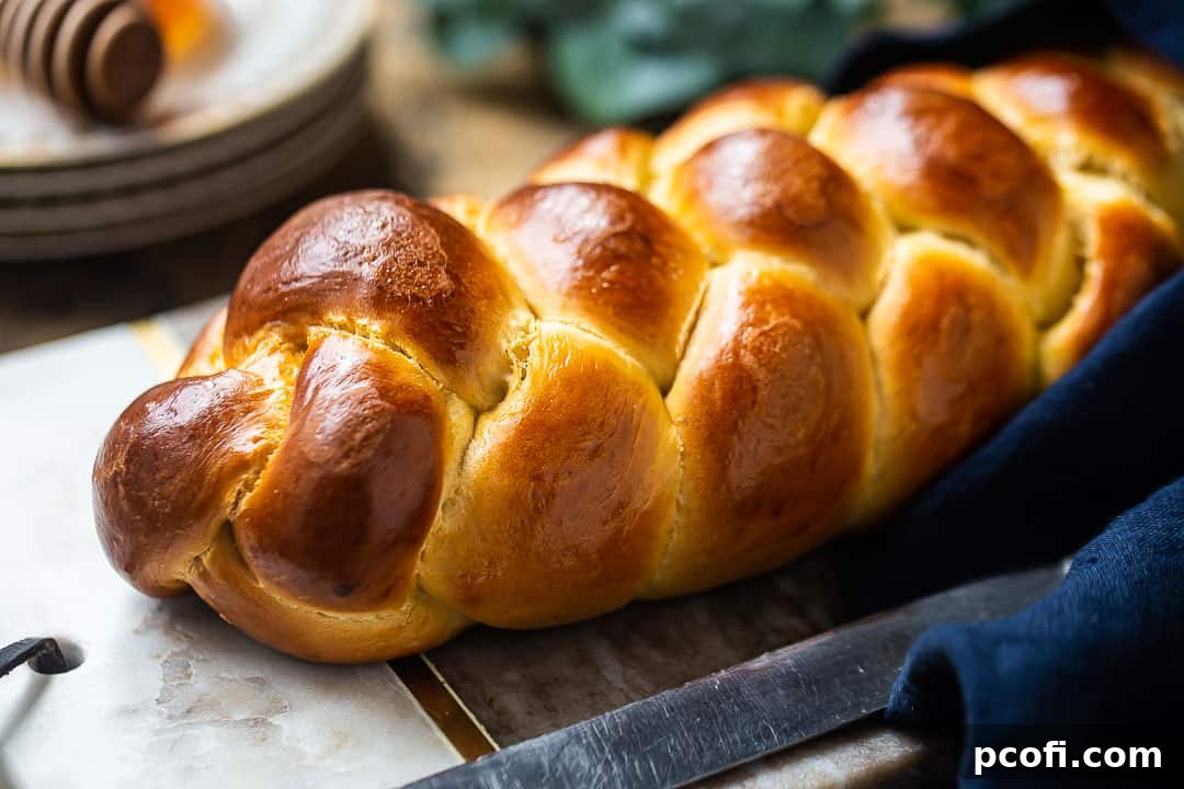Challah bread recipe, baked in a 4-strand braided loaf, presented on a marble serving board.