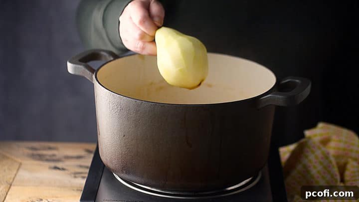 Adding perfectly peeled, firm pears into a pot of gently simmering poaching liquid.
