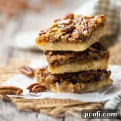 Pecan pie bars stacked on waxed paper, with whole pecans in the background.