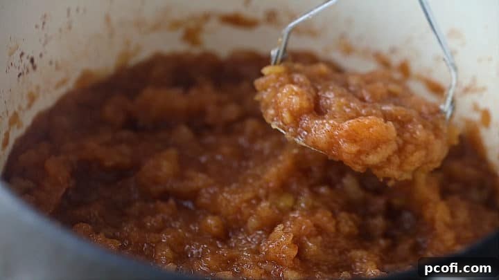 Mashing homemade applesauce with a potato masher for a chunky texture.