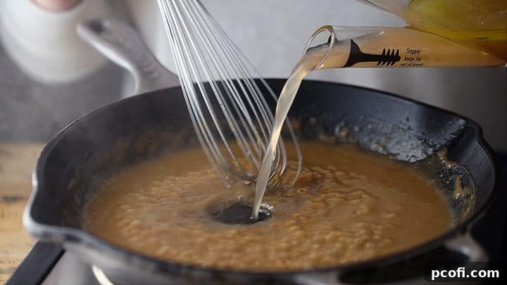 Slowly pouring pan juices into a simmering roux while continuously whisking.