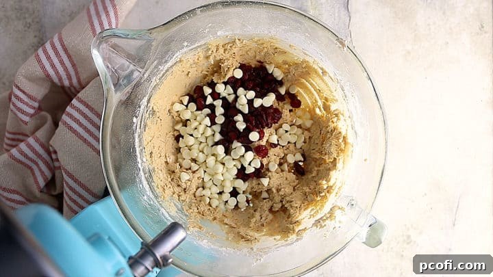 Dried cranberries and white chocolate chips being gently folded into the oatmeal cookie dough.