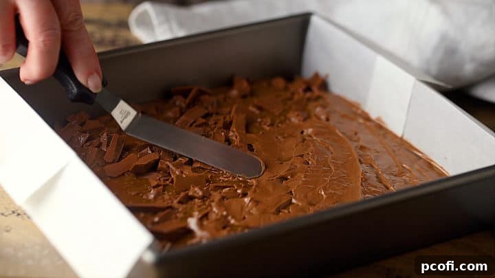 Smoothly spreading the melted chocolate over the homemade toffee with an offset spatula, creating an even layer.