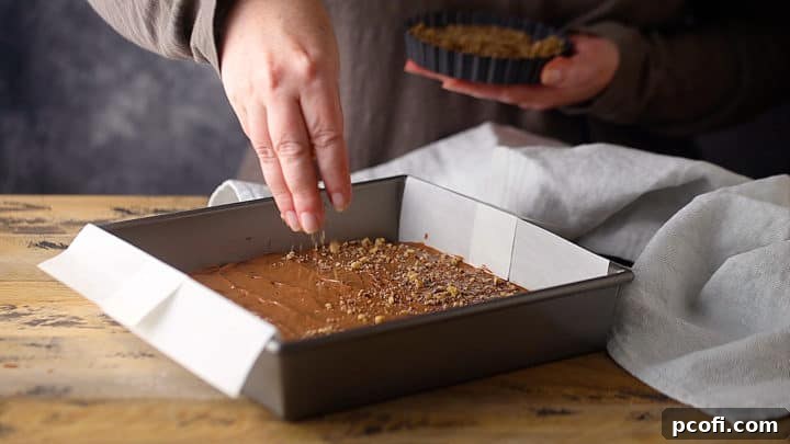 Garnishing the freshly spread chocolate layer on the homemade toffee with a generous sprinkle of finely crushed nuts.