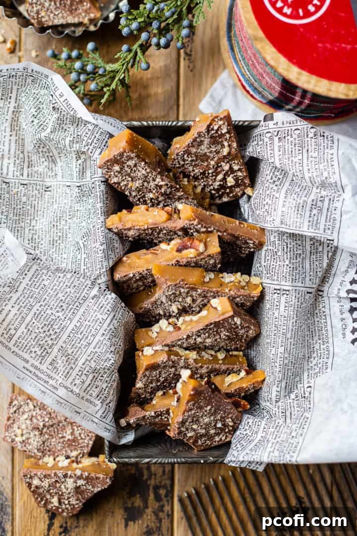An overhead shot showcasing thick, glossy shards of homemade toffee, elegantly arranged in an antique loaf pan, surrounded by festive greenery and a decorative ribbon.