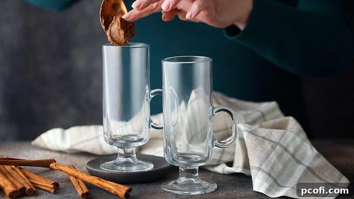 A spoonful of hot buttered rum batter being placed into the bottom of a clear glass serving mug, ready for the next steps.