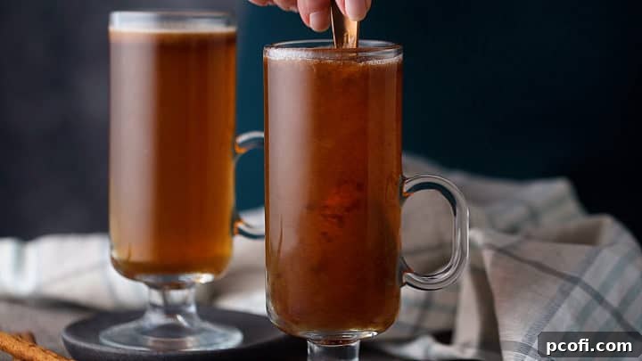 The hot buttered rum is being stirred with a spoon in a glass mug, ensuring the batter fully dissolves and blends with the hot liquid and rum.