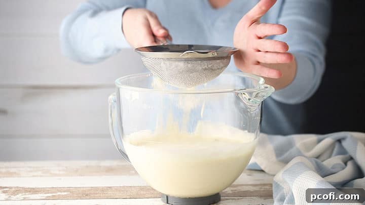 Sifting flour into the airy batter with a fine mesh sieve to prevent lumps and maintain lightness.