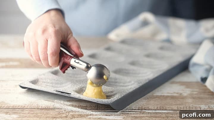 Scooping batter into a perfectly prepared madeleine pan, ensuring each well is filled evenly for uniform baking.