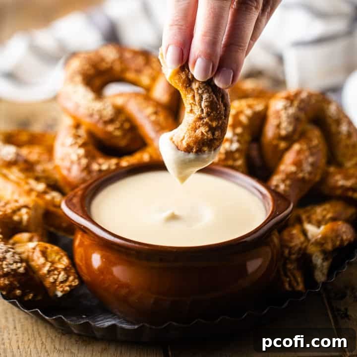 Dipping a homemade soft pretzel into a rich, creamy beer cheese dip, highlighting its perfect texture and golden color.