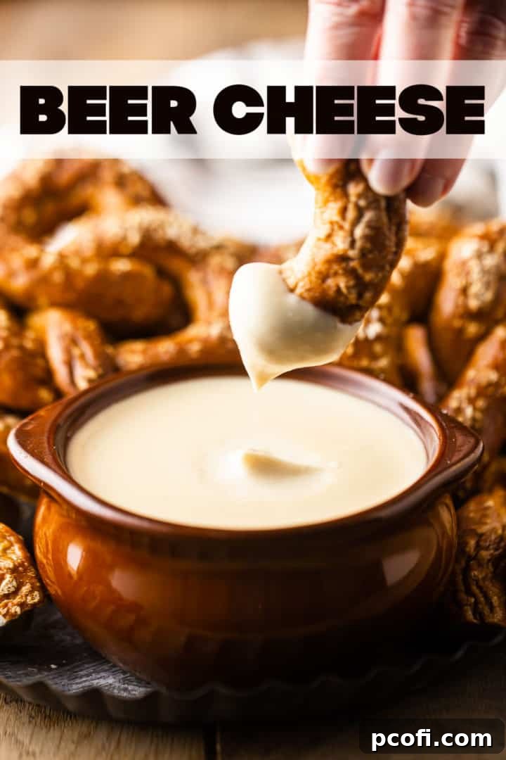 Close-up of a pretzel being dipped into a bowl of luscious beer cheese dip, with a text overlay "Beer Cheese" above, emphasizing its smooth and inviting texture.