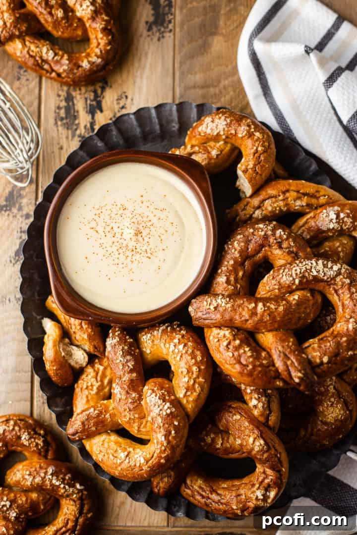 Overhead shot of a rustic brown bowl filled with creamy beer cheese dip, artfully surrounded by golden-brown soft pretzels, ready for dipping.