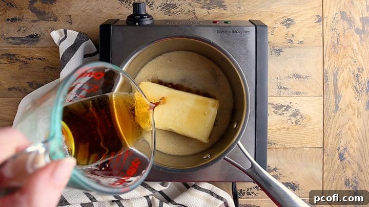 Beer being poured into a small pot containing a block of cream cheese, initiating the melting process for a creamy dip.