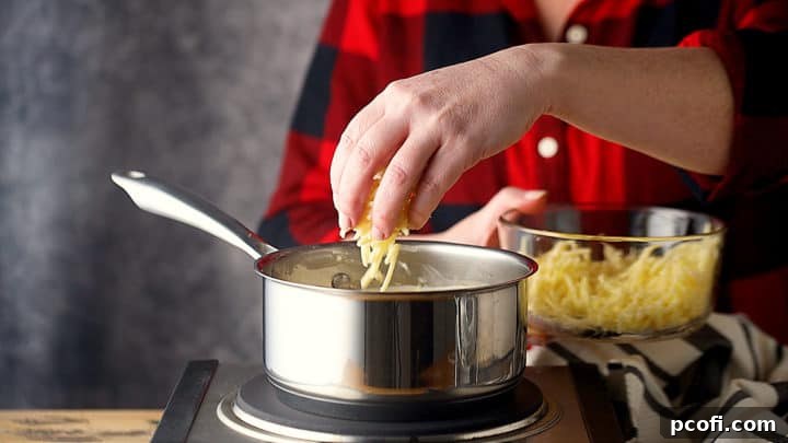 Shredded cheddar cheese being added to the warm cream cheese and beer mixture, ready to be melted and incorporated into the dip.