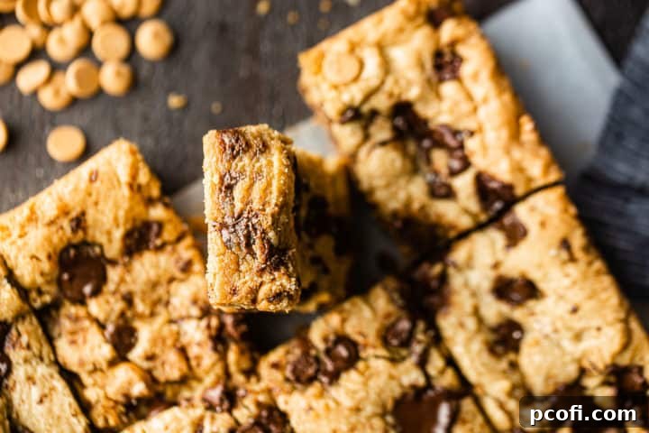 Overhead image of a peanut blondie recipe, cut into squares with one bar tilted up to show the gooey inside.