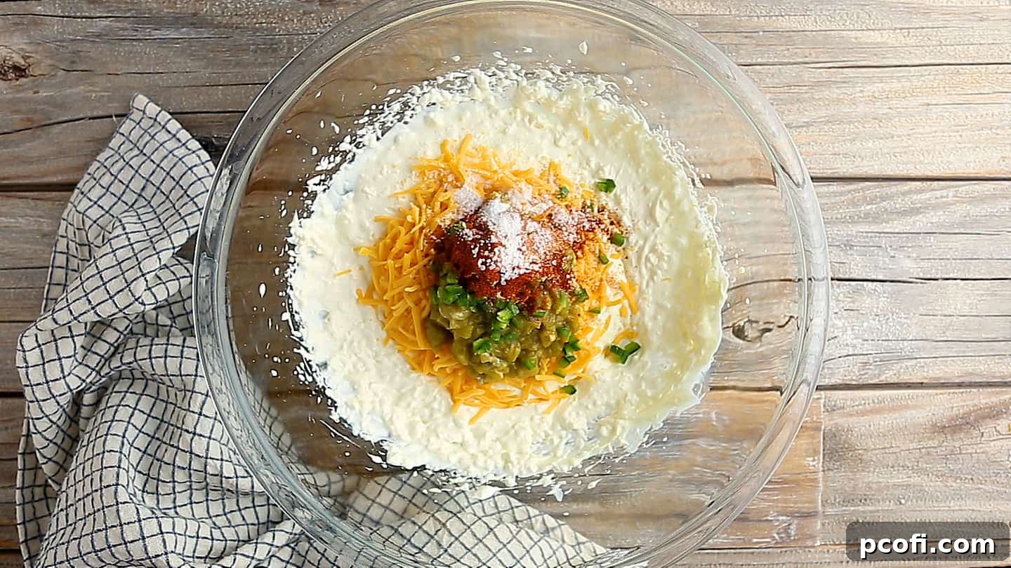 Adding cheddar cheese, diced green chiles, minced fresh jalapeno, salt, garlic powder, and smoked paprika to jalapeno dip recipe.