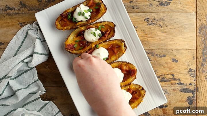 Topping hot, cheesy potato skins with crispy bacon, a dollop of sour cream, and fresh green onions.