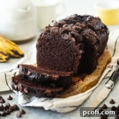 Chocolate banana bread presented on a wooden board with bananas in the background.