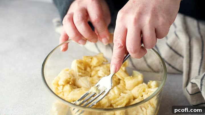 Mashing ripe bananas in a glass bowl with a fork, preparing them for chocolate banana bread batter.