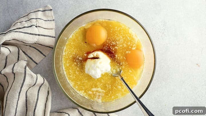 Wet ingredients for chocolate banana bread assembled in a bowl, including mashed bananas, sour cream, milk, eggs, melted butter, and vanilla extract.