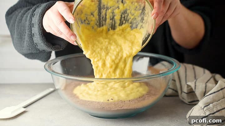 Pouring wet ingredients (mashed bananas, sour cream, milk, eggs, melted butter, vanilla) into the bowl of dry ingredients.