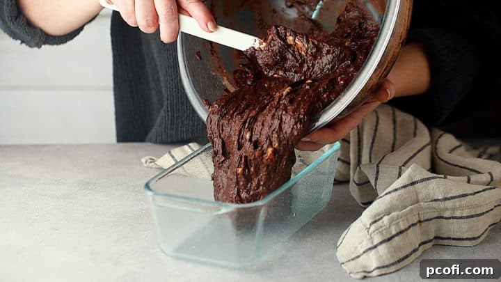 Pouring the thick chocolate banana bread batter into a prepared loaf pan, ready for baking.