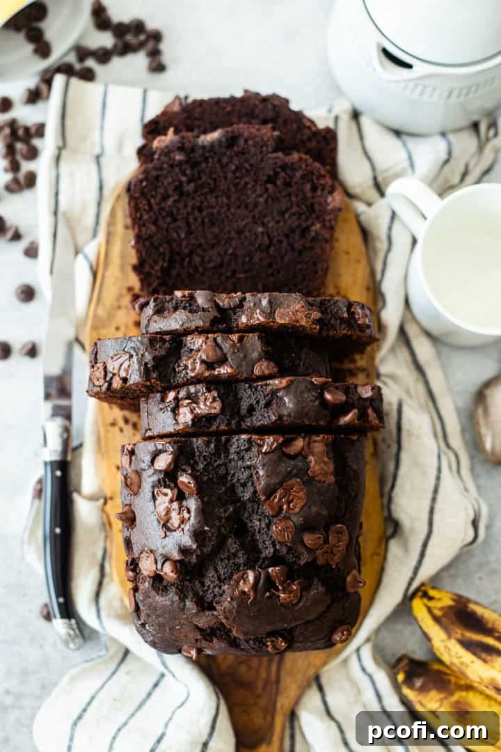 Overhead image of a beautifully sliced chocolate banana bread loaf, surrounded by fresh bananas and loose chocolate chips, showcasing its moist texture.