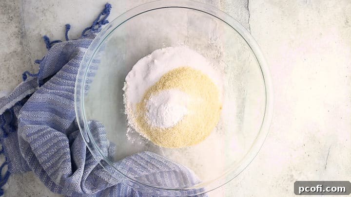 A large glass bowl containing all the dry ingredients for cornbread muffins: flour, sugar, cornmeal, baking powder, and salt.