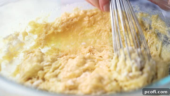 A spatula gently stirring cornbread muffin batter in a large bowl, showing a slightly lumpy consistency.