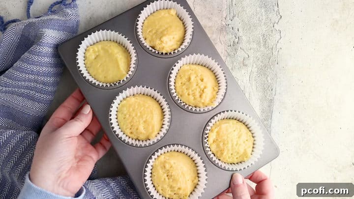 A muffin pan filled with unbaked cornbread muffin batter in paper liners, ready for the oven.