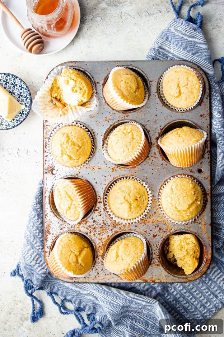 An overhead view of warm cornbread muffins arranged on a vintage pan, accompanied by a jar of honey and a blue kitchen cloth, highlighting their inviting appeal.
