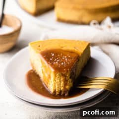 A slice of caramel cheesecake, topped with salted caramel and sea salt, on a white ceramic plate with a gold fork.