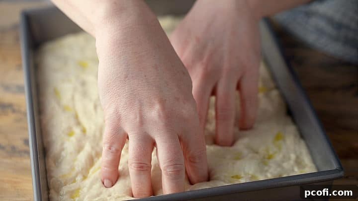 Pushing fingertips into focaccia dough to create dimples.