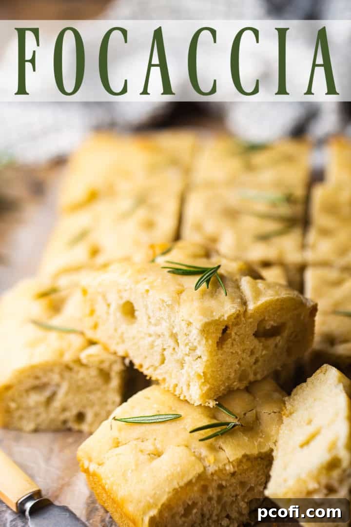 Focaccia bread cut into squares and served on a wooden board with sea salt and rosemary.
