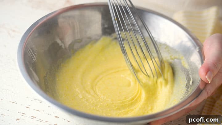 Fresh eggs are being whisked into a dry mixture of cornstarch, sugar, and salt, creating a thick, blended paste.