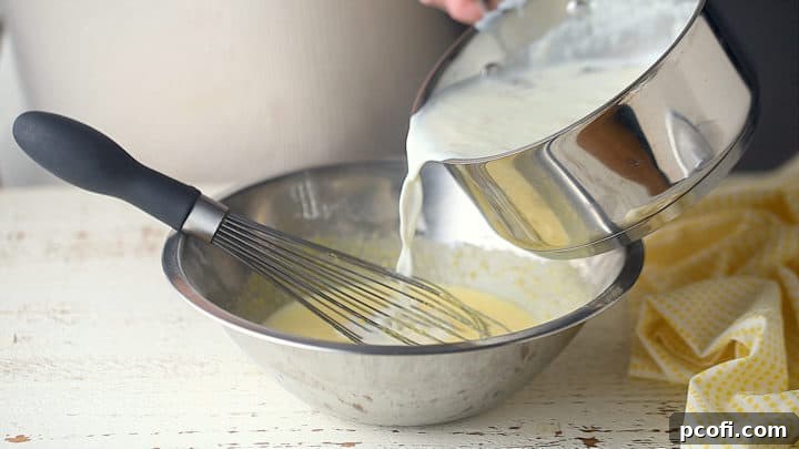 The process of tempering eggs is shown, with hot milk being slowly whisked into the egg mixture to gently raise its temperature.
