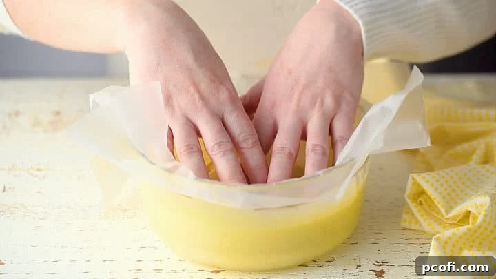 A sheet of plastic wrap is gently pressed directly onto the surface of freshly made homemade pudding, preventing any skin from forming as it cools.