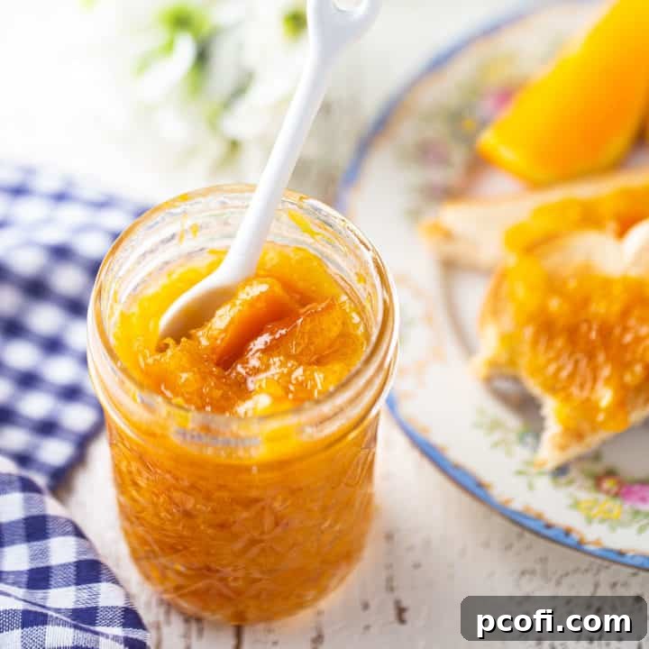 Marmalade in a glass jelly jar with a white ceramic spoon, highlighting the rich texture and vibrant color.