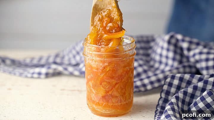 Spooning homemade orange marmalade into sterile jars for canning, ensuring proper headspace for sealing.