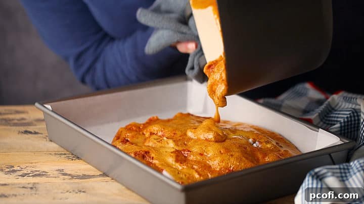 Hot, foamy sponge candy mixture being gently poured into a parchment-lined 9x13 inch pan to cool and harden.