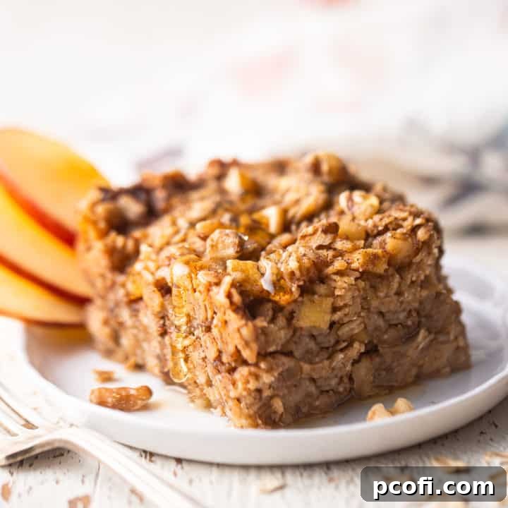 A square of baked oatmeal, served on a white plate with apple slices and honey, emphasizing a comforting breakfast.