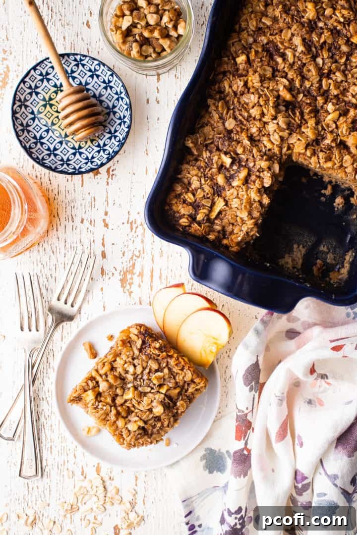 Overhead image of a tray of baked oatmeal with a square cut out and served on a nearby plate, ready to be enjoyed.