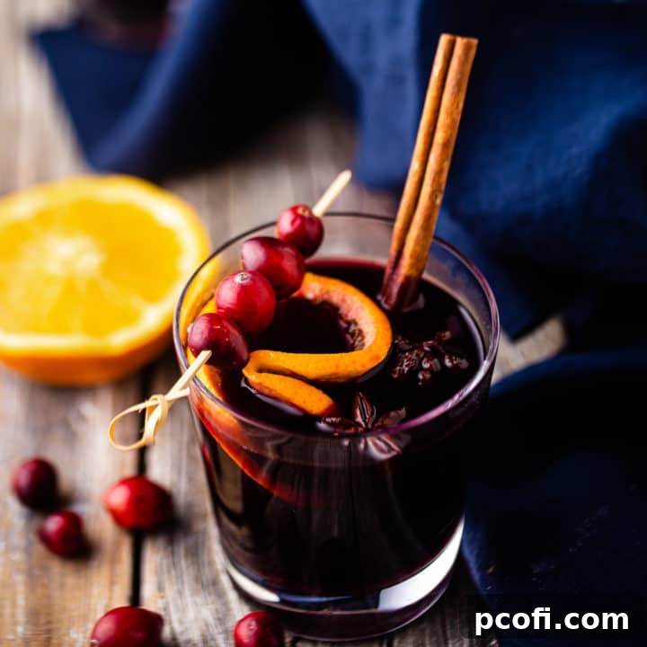 A glass of mulled wine, garnished with a cinnamon stick and fresh cranberries.