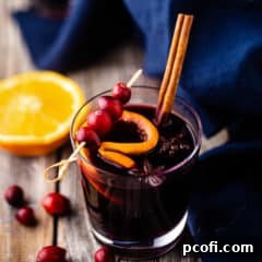 A glass of mulled wine, garnished with a cinnamon stick and fresh cranberries.