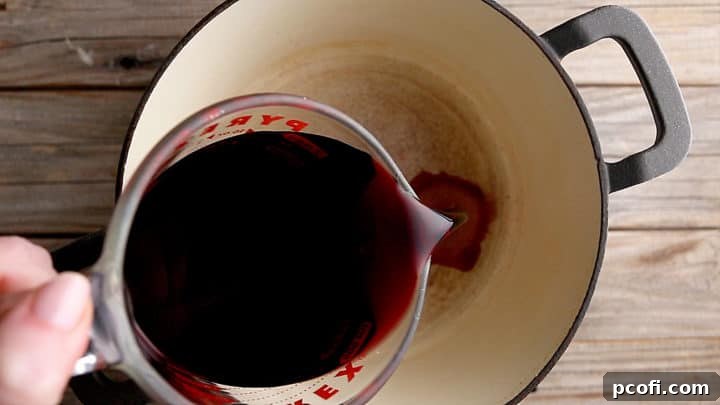 Pouring red wine into a large, heavy-bottomed pot to make mulled wine.