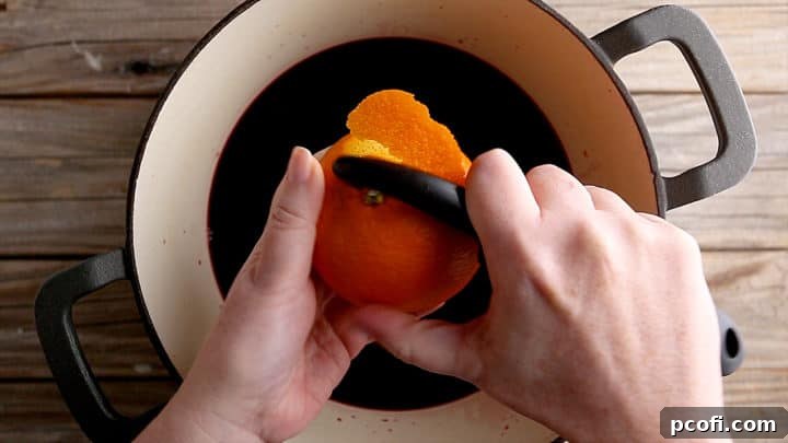Removing the zest from an orange with a veggie peeler.