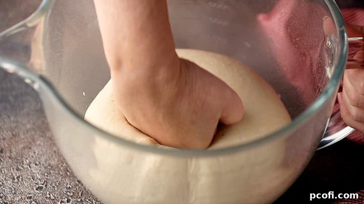 Image of pizza dough being punched down in a mixing bowl after rising, a key step for Detroit-style pizza.