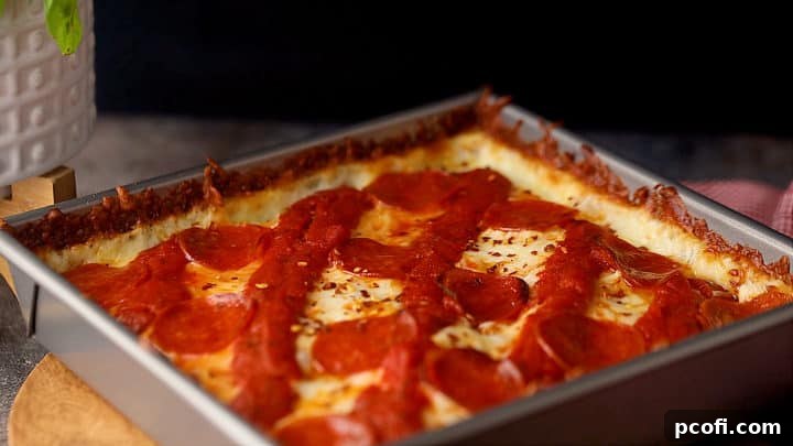 Freshly baked Detroit-style pizza in a square cake pan, showing the golden-brown crust and bubbly cheese.
