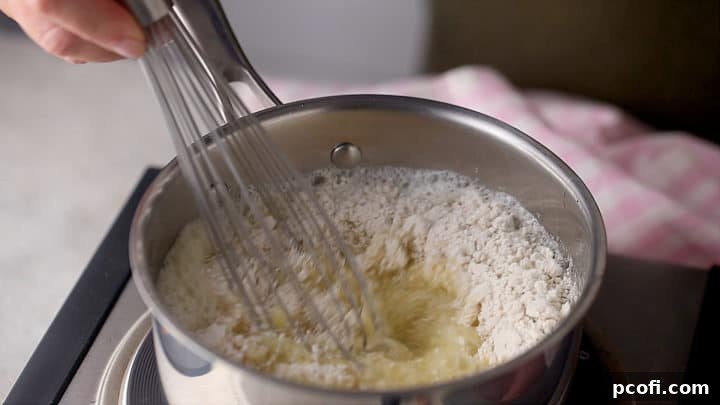 Whisking the flour into the hot liquid to form a smooth choux paste in a saucepan.